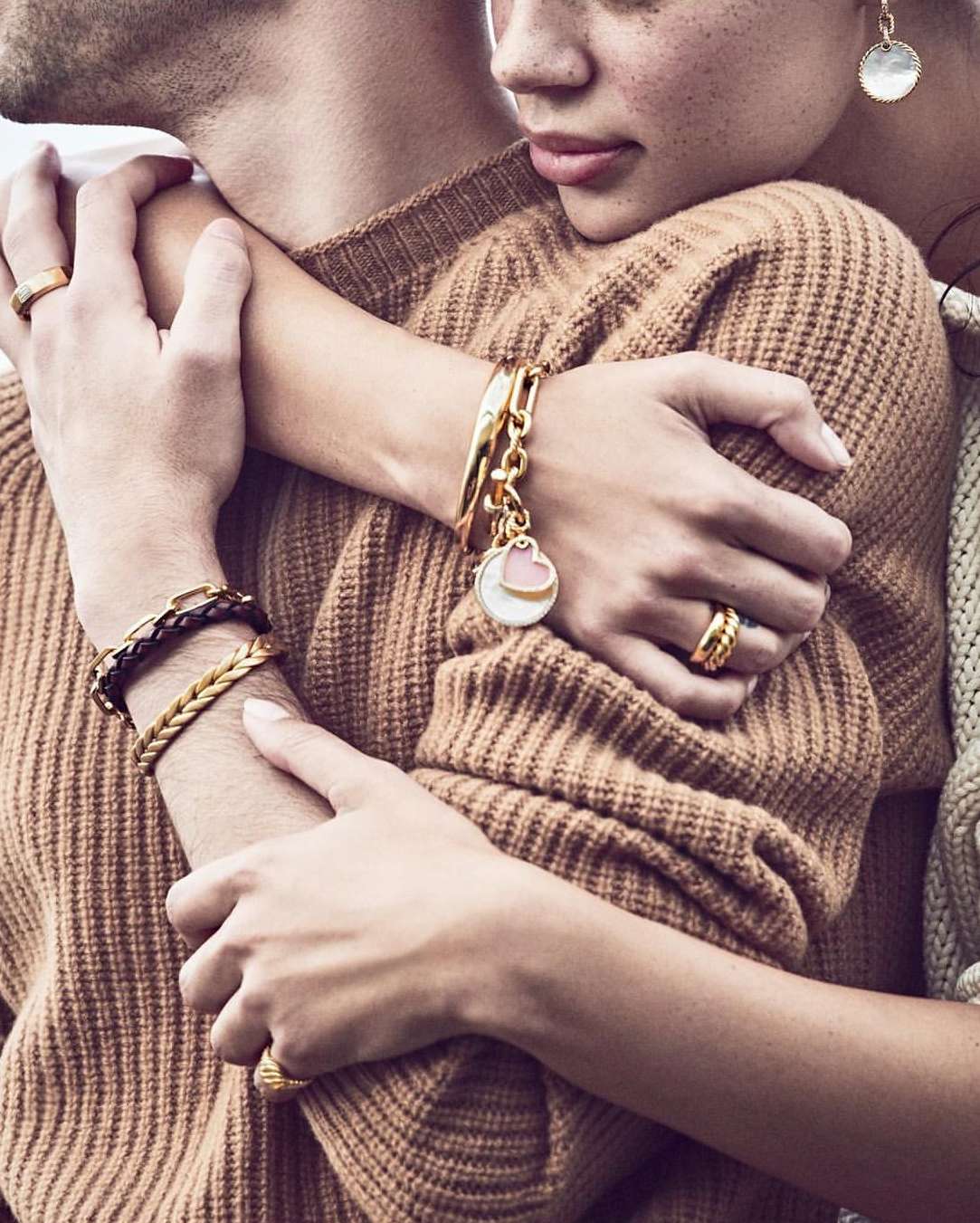 Close-up of a couple embracing, showcasing bracelets and rings. The focus is on the jewelry and the intimate connection between the two people.