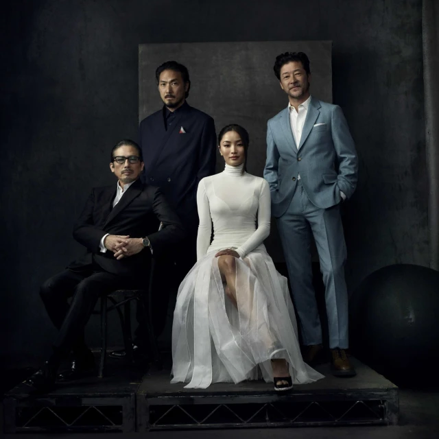 Group portrait of four Asian adults, three men and one woman, formally dressed in suits and a white dress in a studio setting.