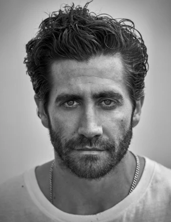 Close-up monochrome portrait of Jake Gyllenhaal with dark wavy hair and beard wearing a white t-shirt