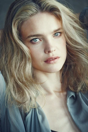 Close-up portrait of a woman with blonde wavy hair and blue eyes wearing a grey top by Matthew Brookes.