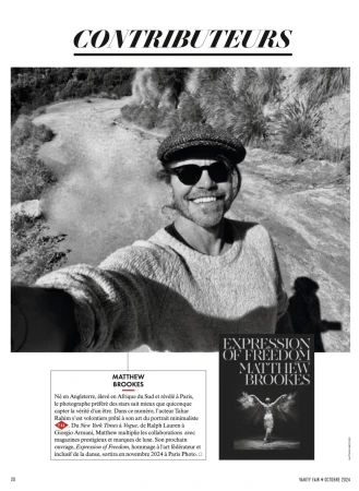 Black and white outdoor portrait of Matthew Brookes wearing sunglasses and a cap, smiling in front of a pale textured background.