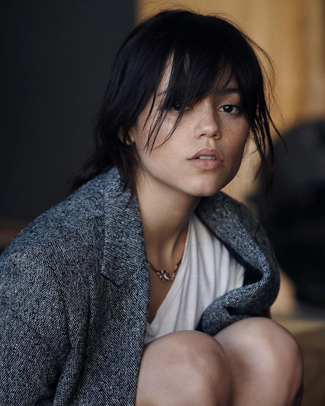 Portrait of young woman with dark hair and freckles wearing a grey tweed blazer and white t-shirt