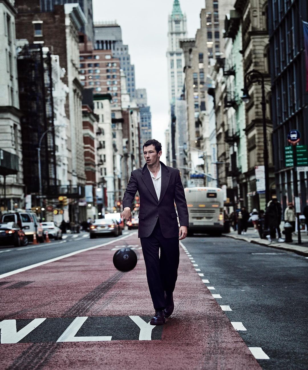 Young man in suit dribbles basketball in city street, surrounded by tall buildings and urban scene. Stylish and athletic concept.