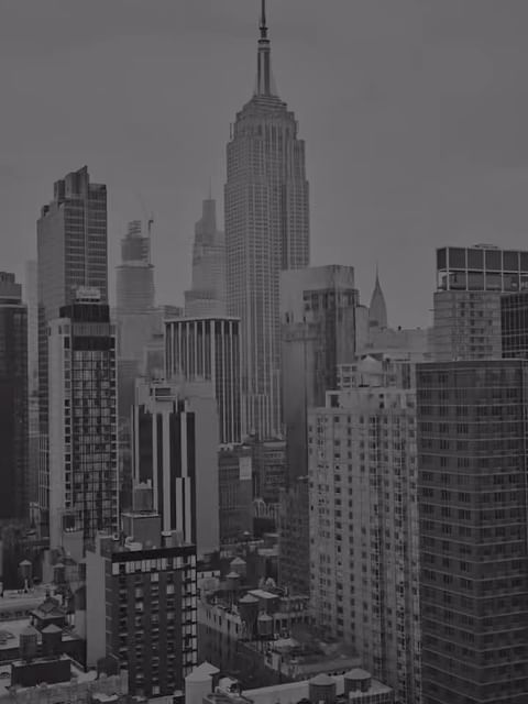 Monochrome cityscape featuring the Empire State Building amidst surrounding skyscrapers under an overcast sky in an urban environment.