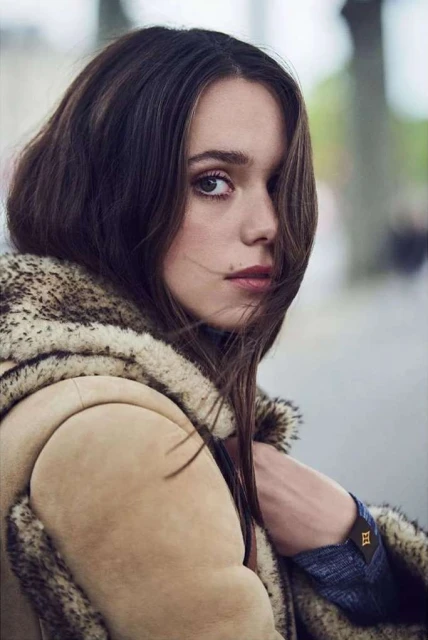 Close-up portrait of an adult woman with dark brown hair and light skin, wearing a patterned jacket, gazing intently at the viewer.
