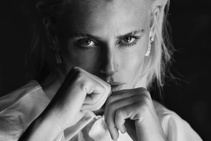 Close up monochrome portrait of a woman with her fists raised wearing a white shirt and drop earrings