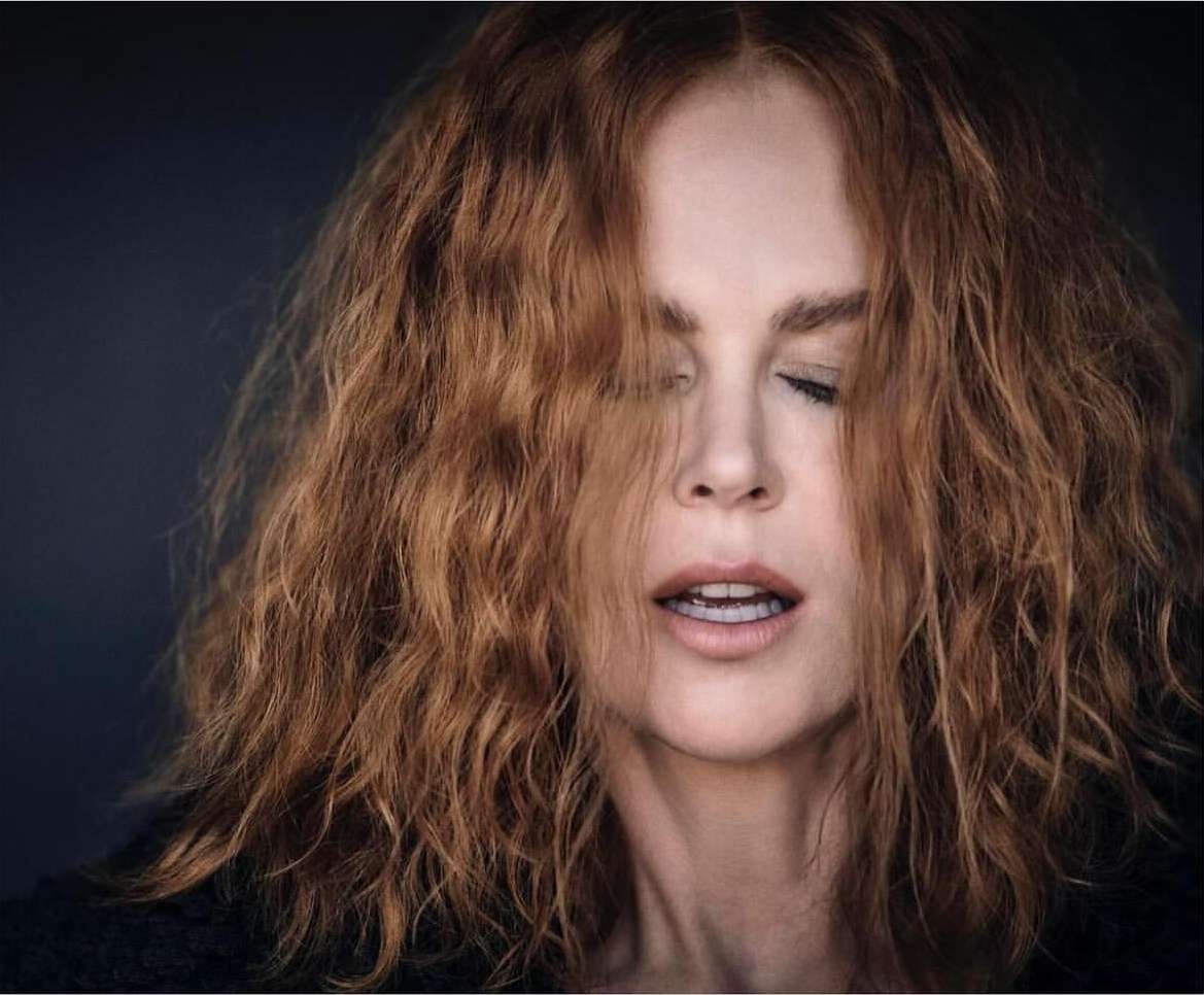 Close-up portrait of a woman with shoulder-length wavy red hair and closed eyes, shot by Matthew Brookes against a dark background.