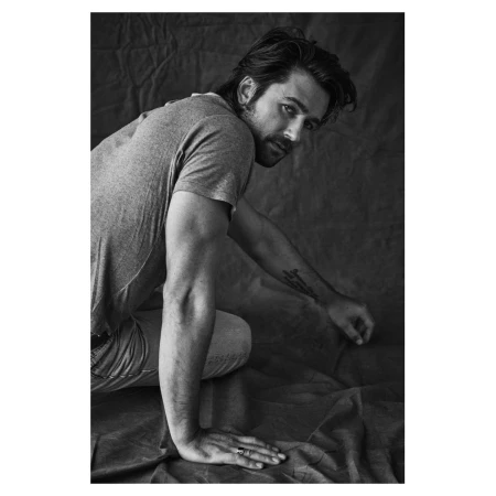 Monochrome portrait of a man kneeling on a textured fabric backdrop wearing a t-shirt and jeans