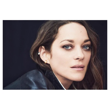 Close-up portrait of Marion Cotillard with dark hair and blue eyes, wearing a black jacket against a dark background.