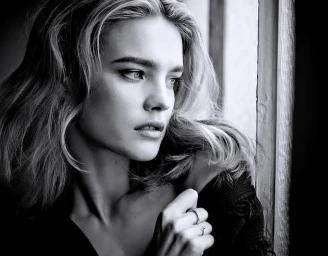 Black and white portrait of a woman looking out a window wearing rings on her fingers