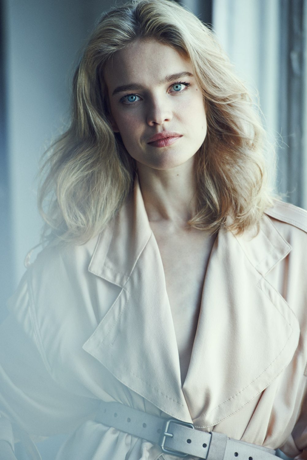 Portrait of a blonde woman wearing a light beige belted trench coat, directed by Matthew Brookes.