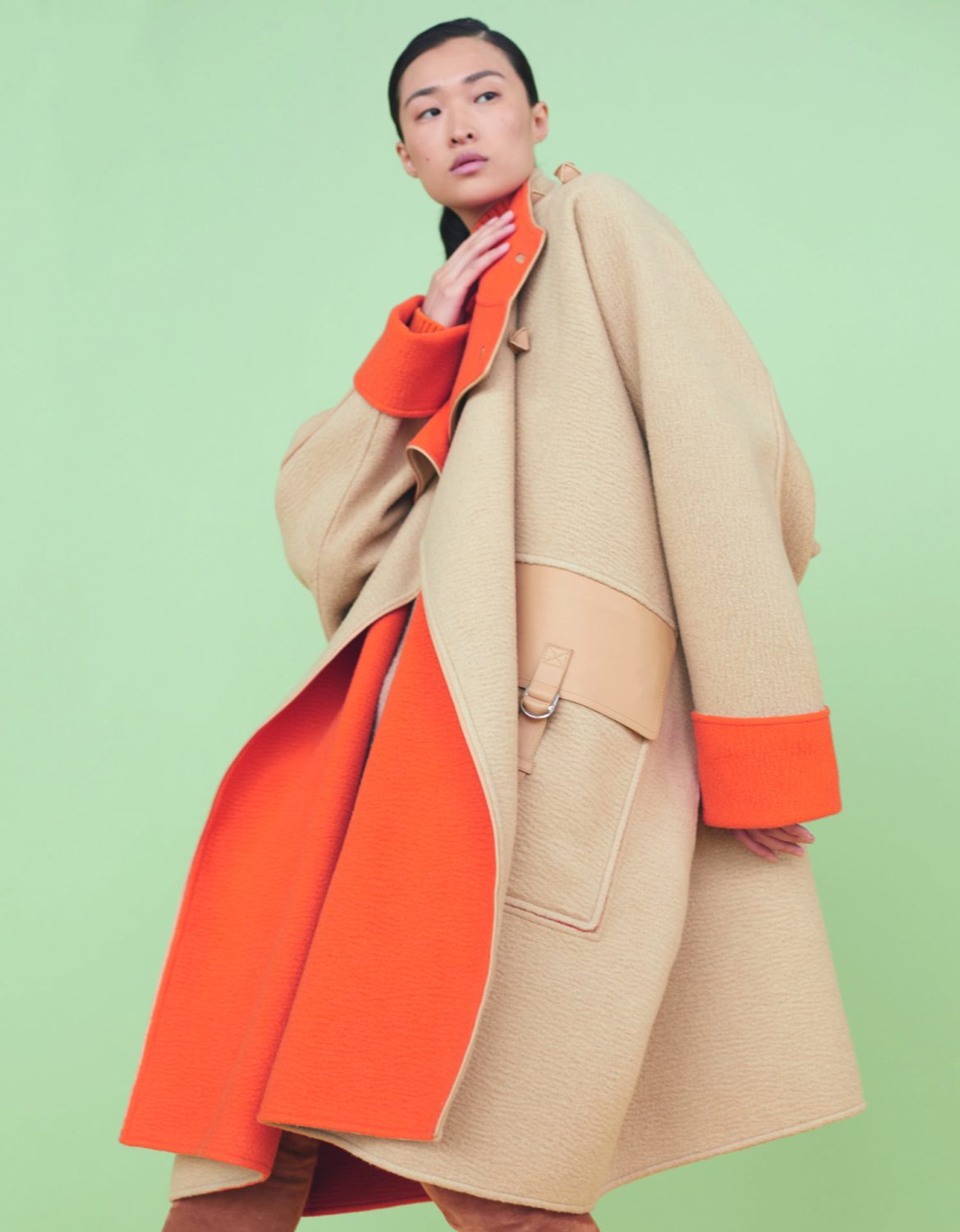 Model wearing a beige and orange coat with matching cuffs against a solid green background