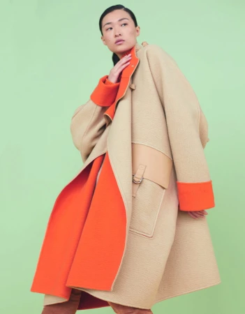 Model wearing a beige and orange coat with matching cuffs against a solid green background