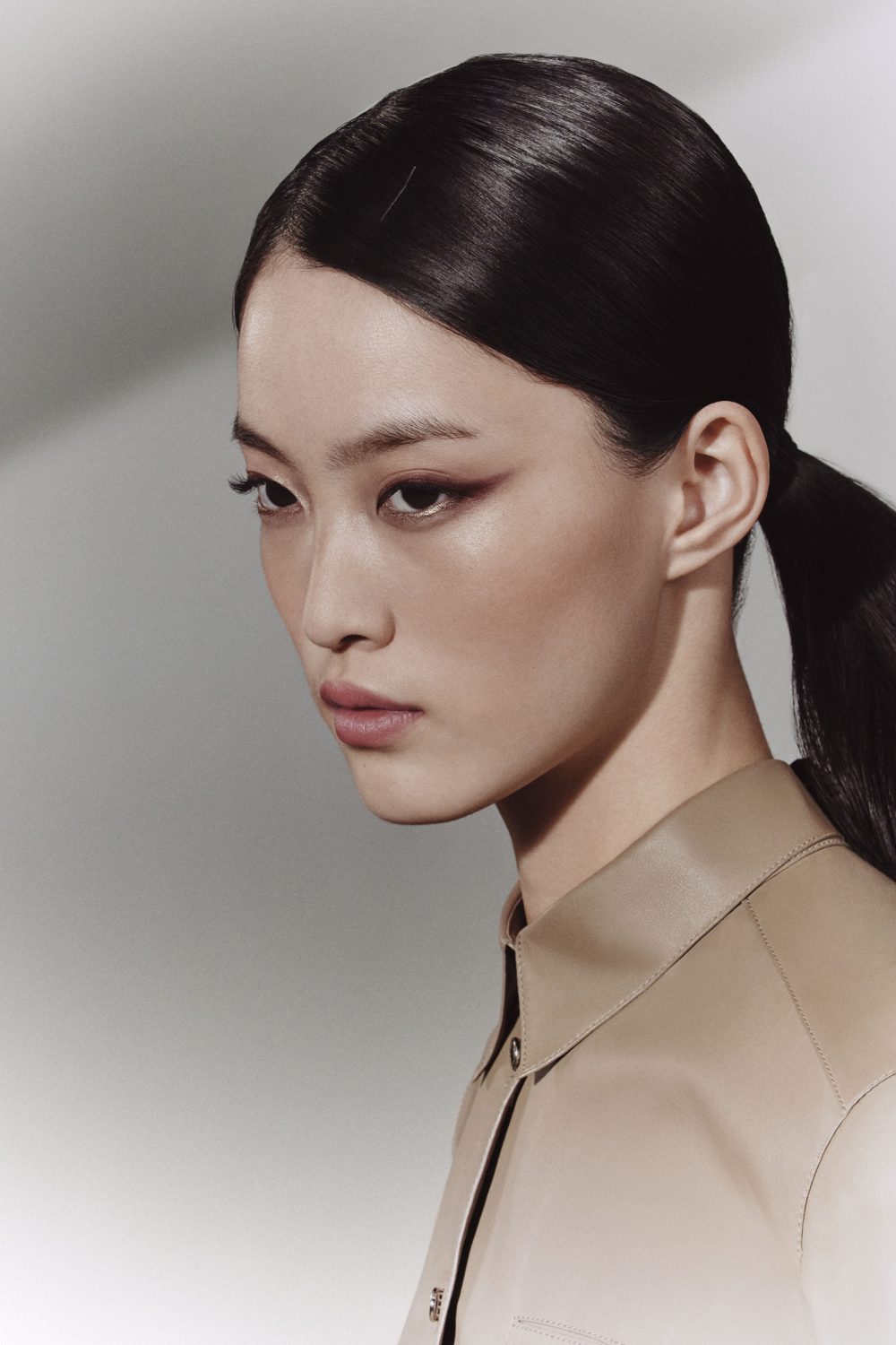 Close-up portrait of an East Asian woman with dark sleek hair in a ponytail wearing a beige button-down shirt