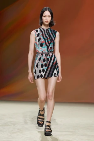 Model walking the runway wearing a sleeveless patterned mini dress and black strappy platform sandals