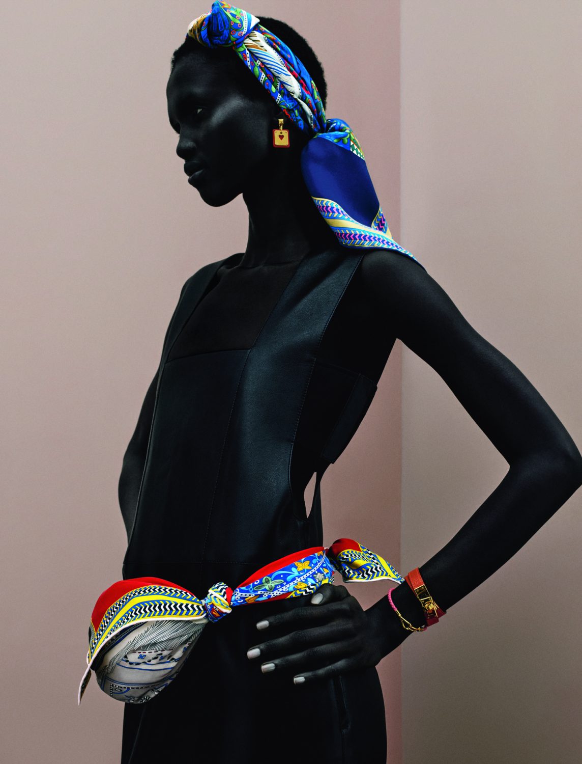 Woman in a black dress posing with a printed headscarf and waist scarf. Shot in a photo studio with a simple background.