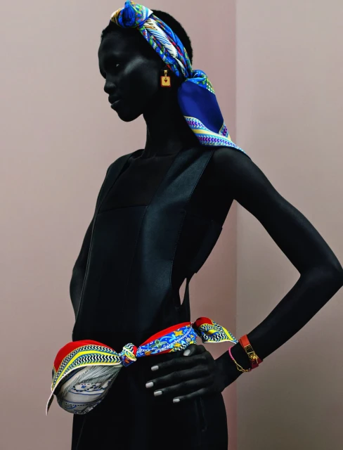 Woman in a black dress posing with a printed headscarf and waist scarf. Shot in a photo studio with a simple background.