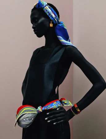 Woman in a black dress posing with a printed headscarf and waist scarf. Shot in a photo studio with a simple background.