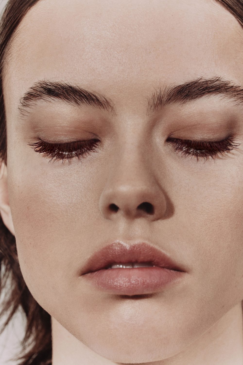 Close-up portrait of a young adult woman with fair skin, closed eyes, and light pink lips, bathed in soft, diffused lighting.
