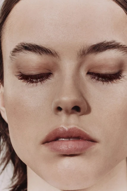 Close-up portrait of a young adult woman with fair skin, closed eyes, and light pink lips, bathed in soft, diffused lighting.
