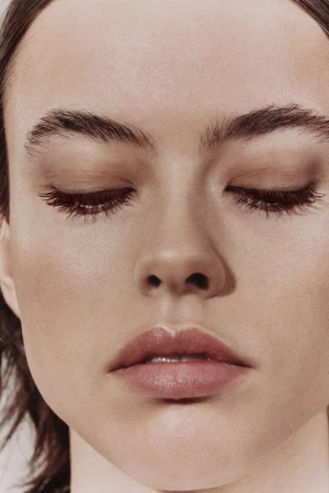 Close-up portrait of a young adult woman with fair skin, closed eyes, and light pink lips, bathed in soft, diffused lighting.