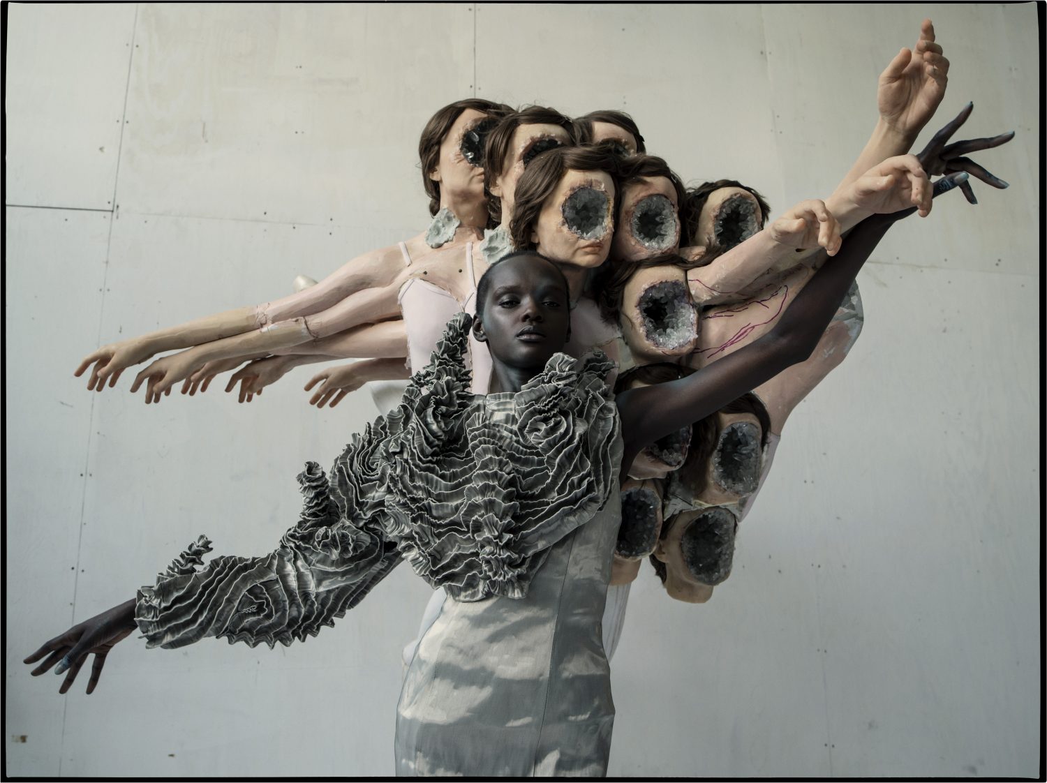 Artistic fashion shot featuring a dark-skinned model in a ruffled top, surrounded by mannequin parts and set against a plain studio backdrop.