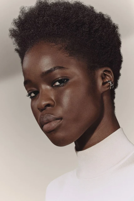 Close-up portrait of a young black woman with natural hair and a white top, showcasing a star-shaped ear cuff in a softly lit studio setting.