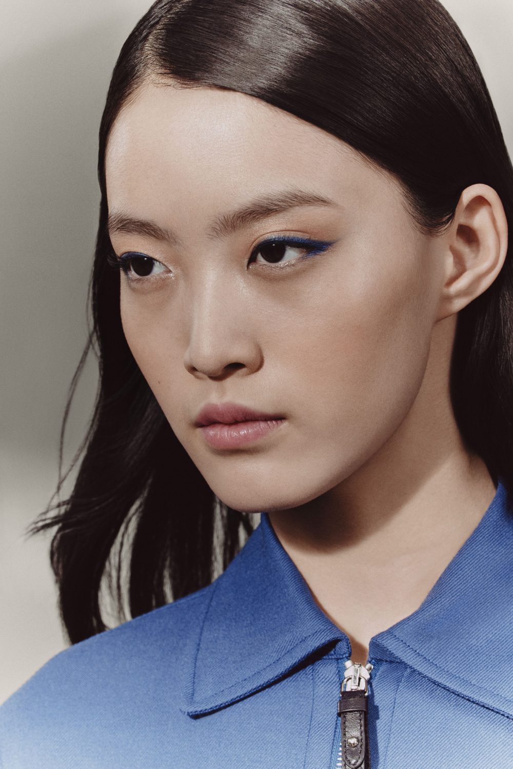 Close-up shot of a woman with dark hair and blue eyeliner, wearing a blue top. Beauty shot with a focus on makeup and facial features.