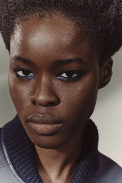 Close-up shot of an African American woman with blue eyeliner, wearing a blue collared jacket, and posing in a photo studio.