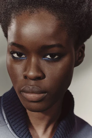 Close-up shot of an African American woman with blue eyeliner, wearing a blue collared jacket, and posing in a photo studio.