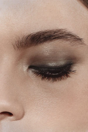 Close-up studio shot of a woman's closed eye featuring dark eye shadow, long eyelashes, and a neatly shaped eyebrow.