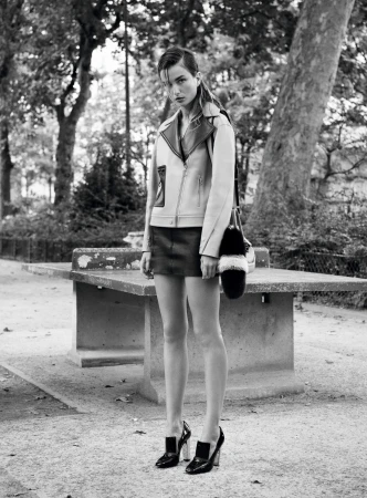 Black and white portrait of a model wearing a leather jacket and skirt standing outdoors near a park table.