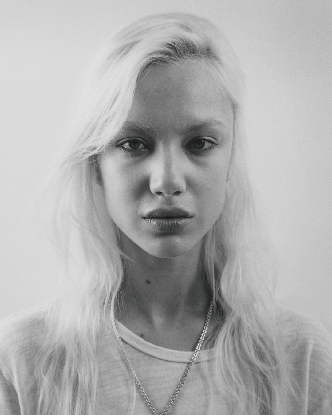 Portrait of a young blonde woman with long hair and a light t-shirt against a plain background