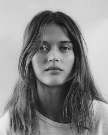 Close-up portrait of a woman with long hair and neutral expression against a plain white background