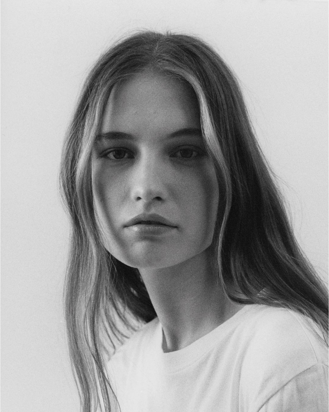 Black and white portrait of a young woman with long hair wearing a white t-shirt against a plain background