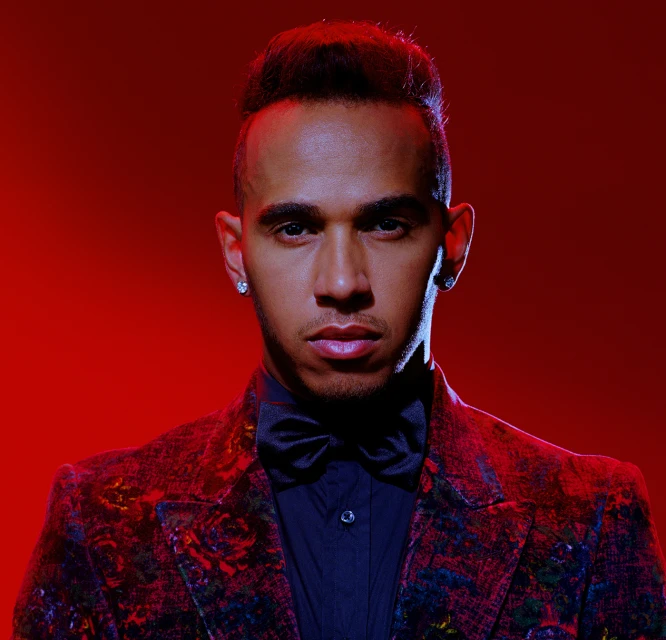 Portrait of Lewis Hamilton in a dark suit and bow tie against a red background, showcasing his elegant and serious demeanor.