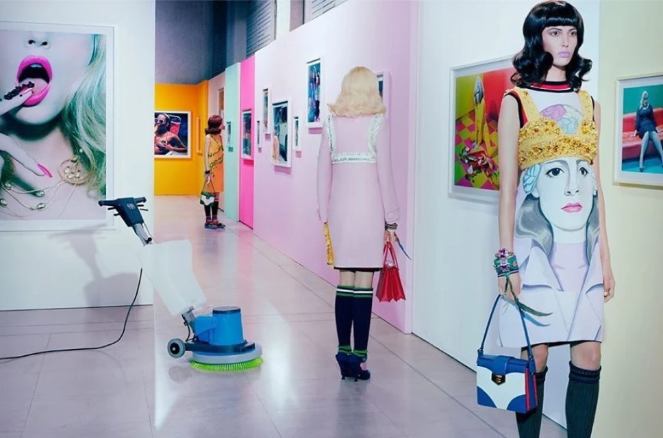Art gallery scene with mannequins dressed in illustrated dresses, framed artwork on the walls, and a floor cleaning machine.