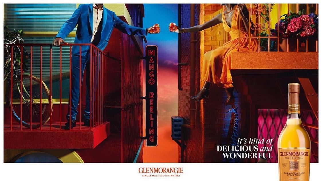 Whiskey ad featuring a smartly dressed man and woman on balconies, toasting with orange drinks, product visible in the foreground.