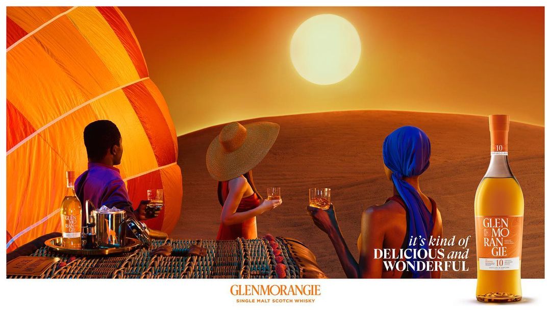 Glenmorangie Scotch whiskey ad featuring three people in a hot air balloon over a desert landscape at sunset, with a bottle of whiskey.