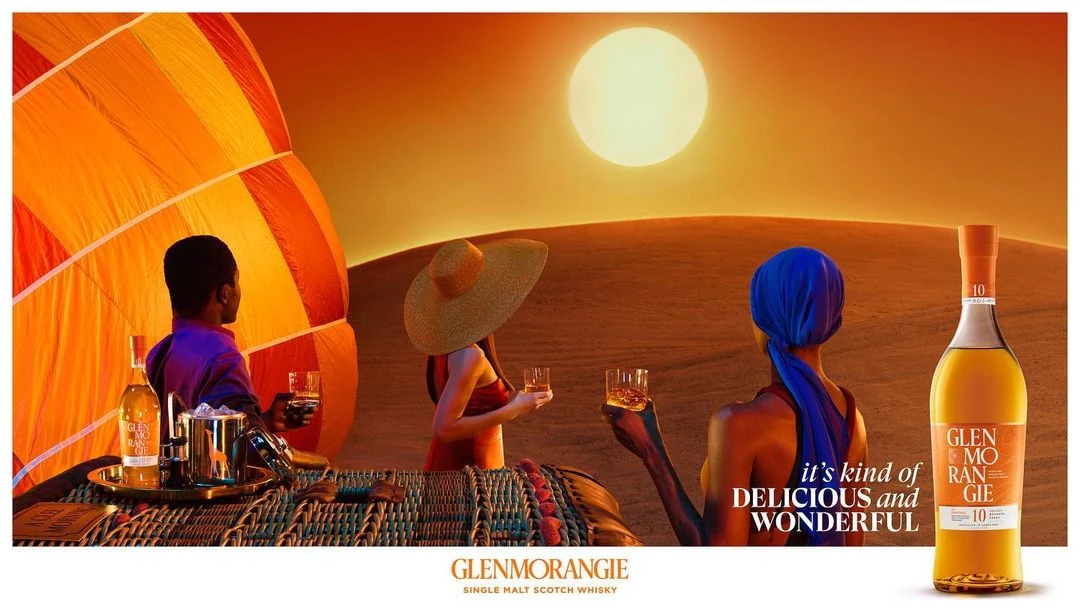 Glenmorangie Scotch whiskey ad featuring three people in a hot air balloon over a desert landscape at sunset, with a bottle of whiskey.
