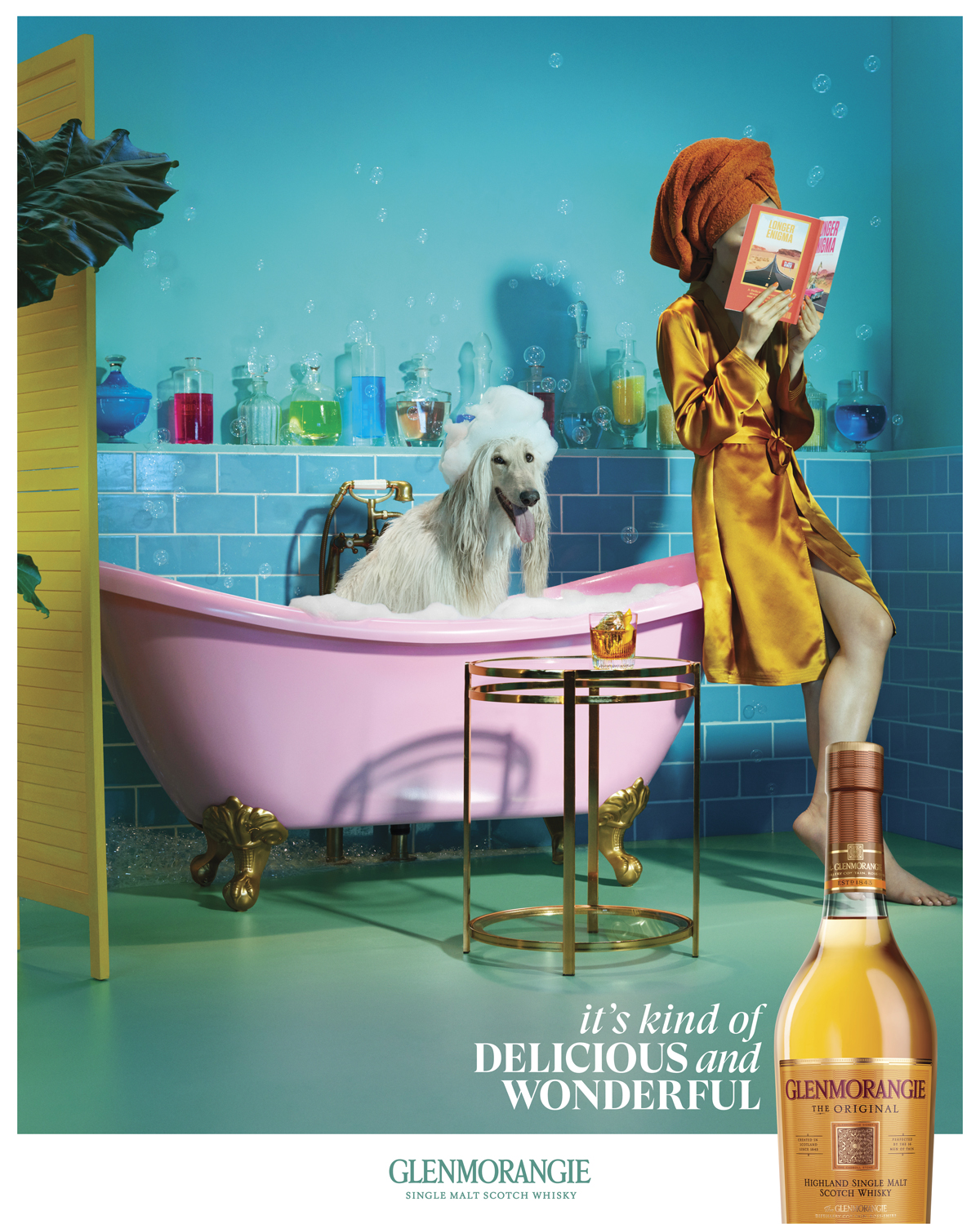 Eye-level shot of an Afghan hound dog in a pink tub, accompanied by a woman in a gold robe reading. The shot is a brand advertisement.