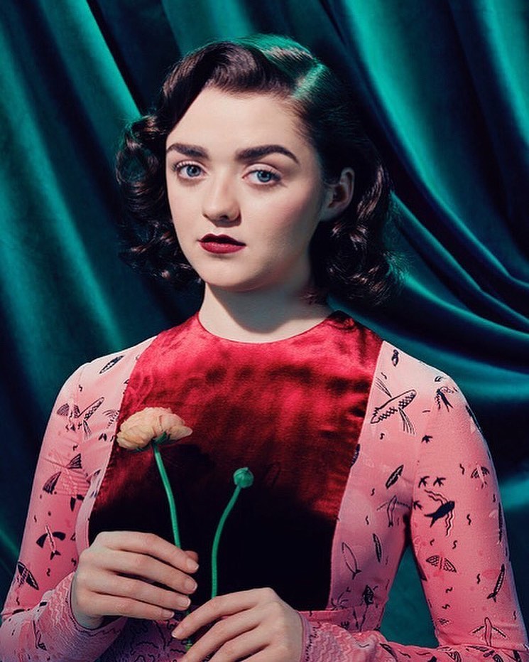 Portrait of a woman with dark hair and a patterned dress, holding a flower, with a turquoise curtain backdrop in a photo studio.