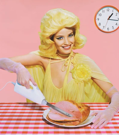 Woman with retro blonde hairstyle slices ham on gingham tablecloth under clock against pink background in stylized, colorful studio shot.