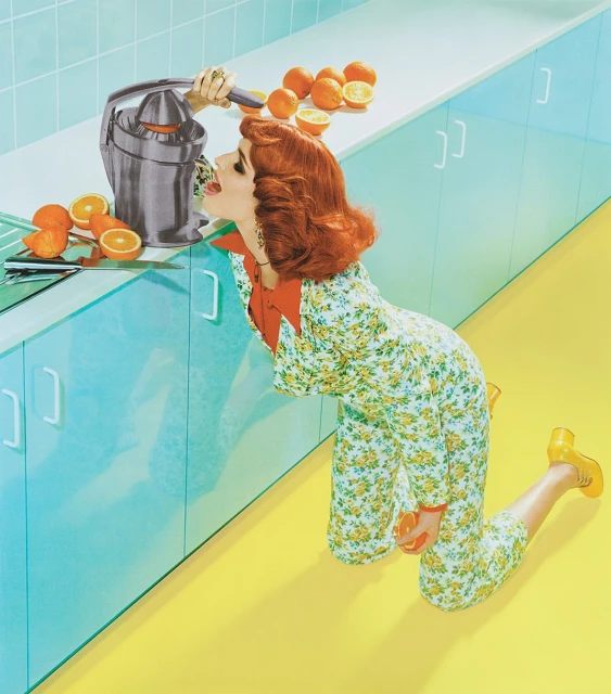 Red-haired woman in floral pajamas uses a vintage-style juicer on a counter full of oranges in a brightly coloured kitchen.