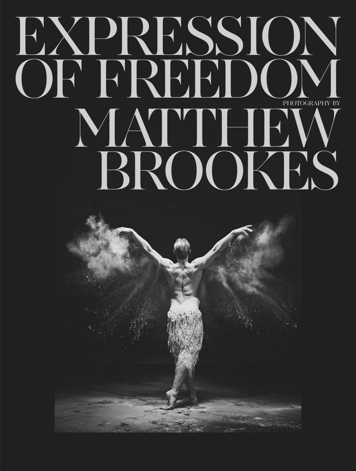 A ballet dancer strikes a pose with arms spread and powdered substance around them in a black and white shot for editorial use.