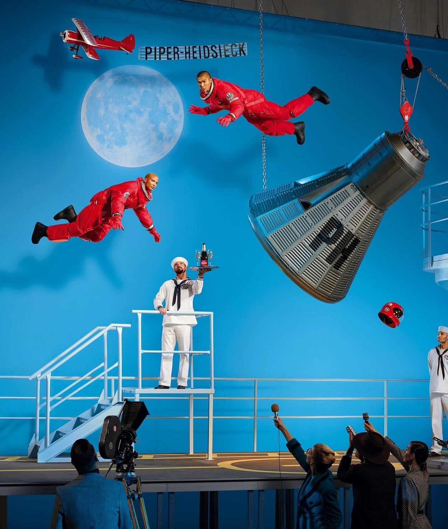 Nautical-themed surreal stage production with model actors, airplane, and a spacecraft hanging from chains.