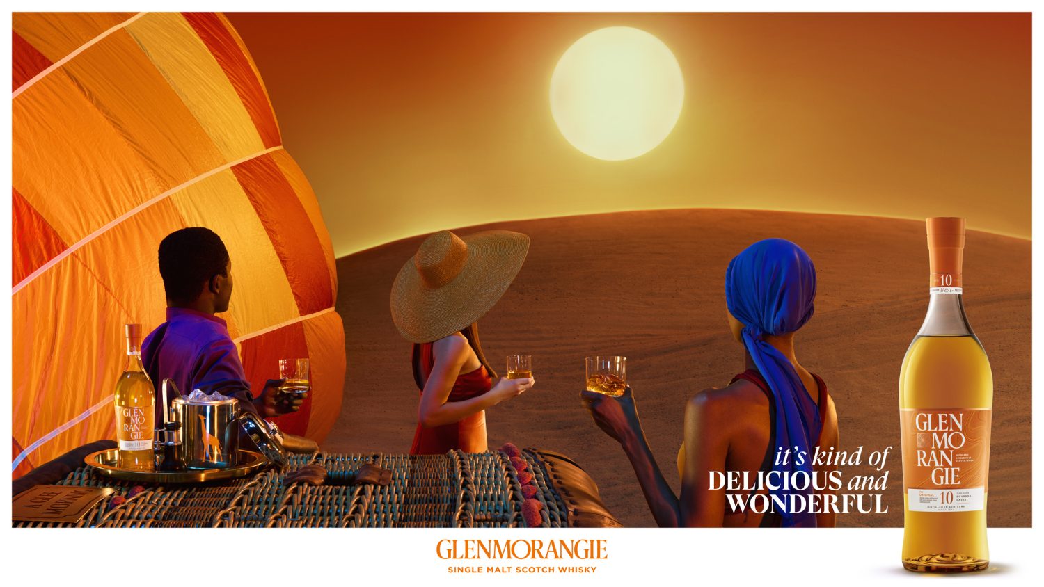Glenmorangie scotch whisky ad: people in hot air balloon enjoying drinks, sun setting over desert sand dunes, bottle displayed.