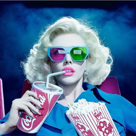 Blonde woman with 3D glasses in a theater, drinking Coca-Cola and holding popcorn, under blue lighting with smoke effect.