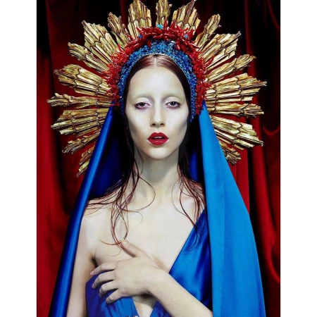 Woman in a blue robe and ornate headpiece in a portrait with a red curtain background. High fashion and beauty shot.