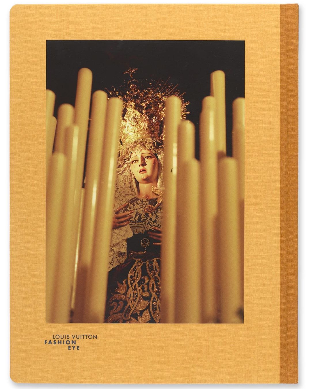 Photograph of a religious icon figure framed by lit candles, featured on the cover of a Louis Vuitton Fashion Eye book with a tan cover.